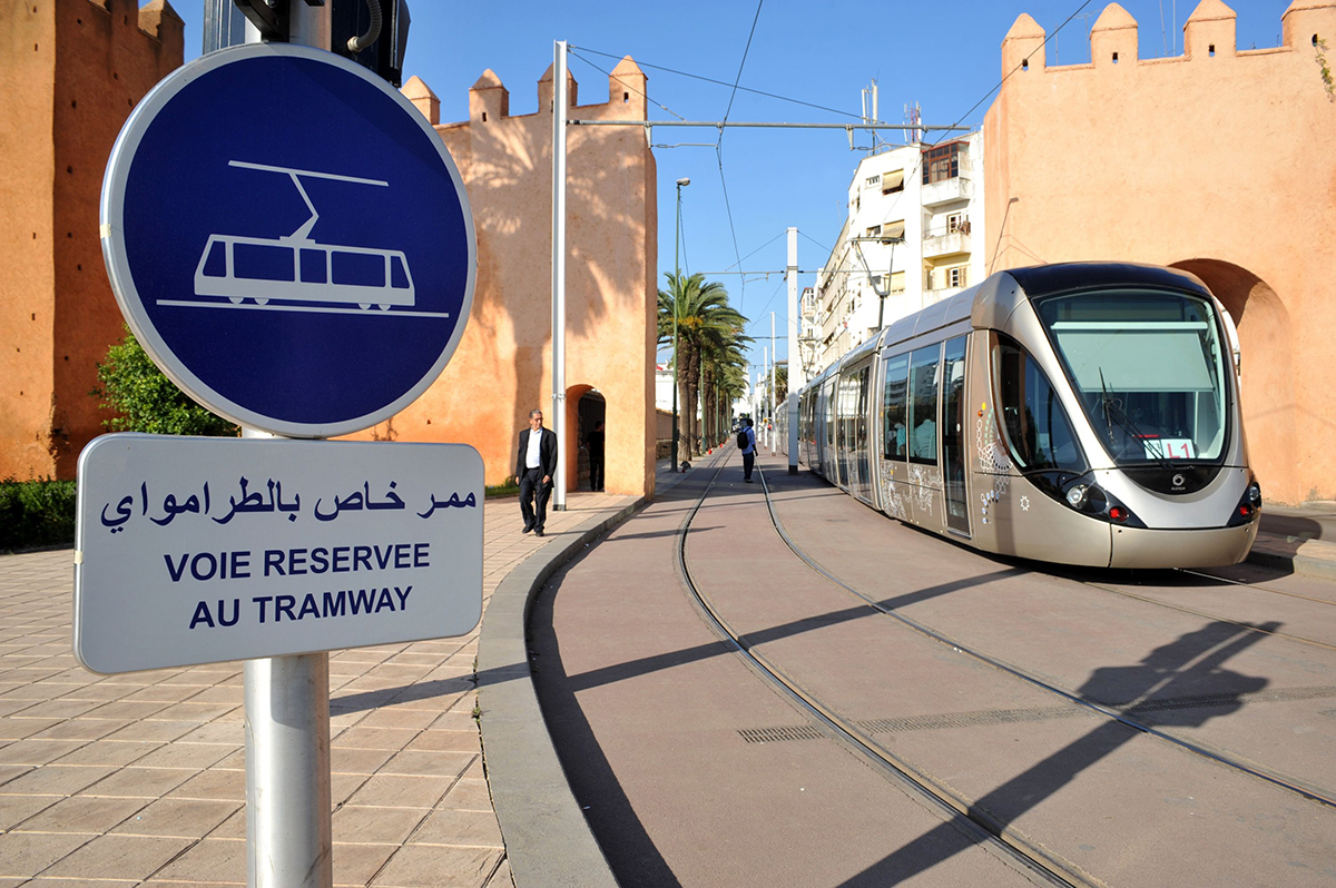 Tramway circulant sur une voie réservée, avec des panneaux en français et en arabe, dans un décor urbain et architectural typique.