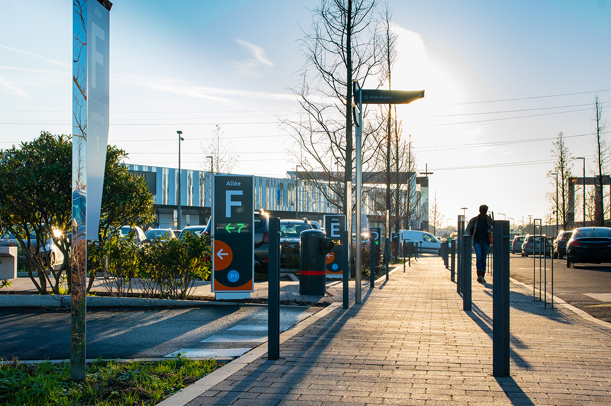 Allée dans un parking et un homme marchant le long d'un chemin pavé sous un ciel clair.